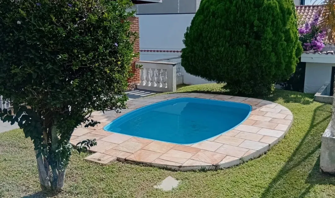 Piscina com borda de pedra no meio de um gramado aparado, com árvores podadas em volta